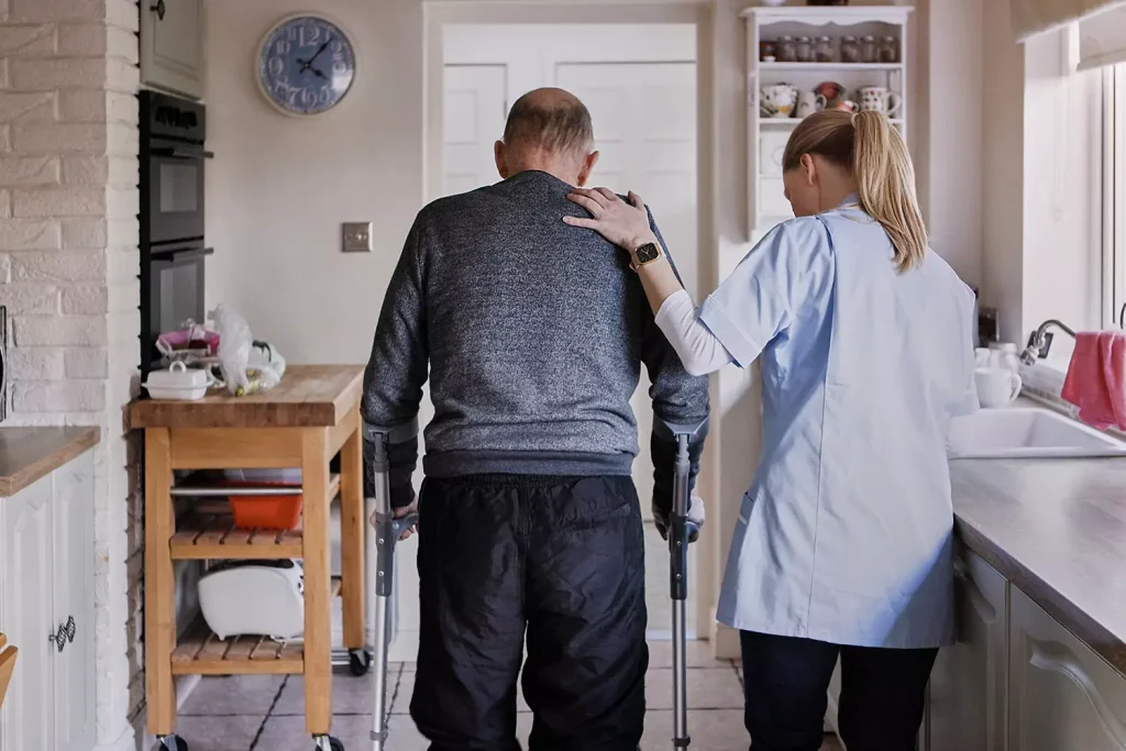 An elderly man is being helped by a nurse in his home